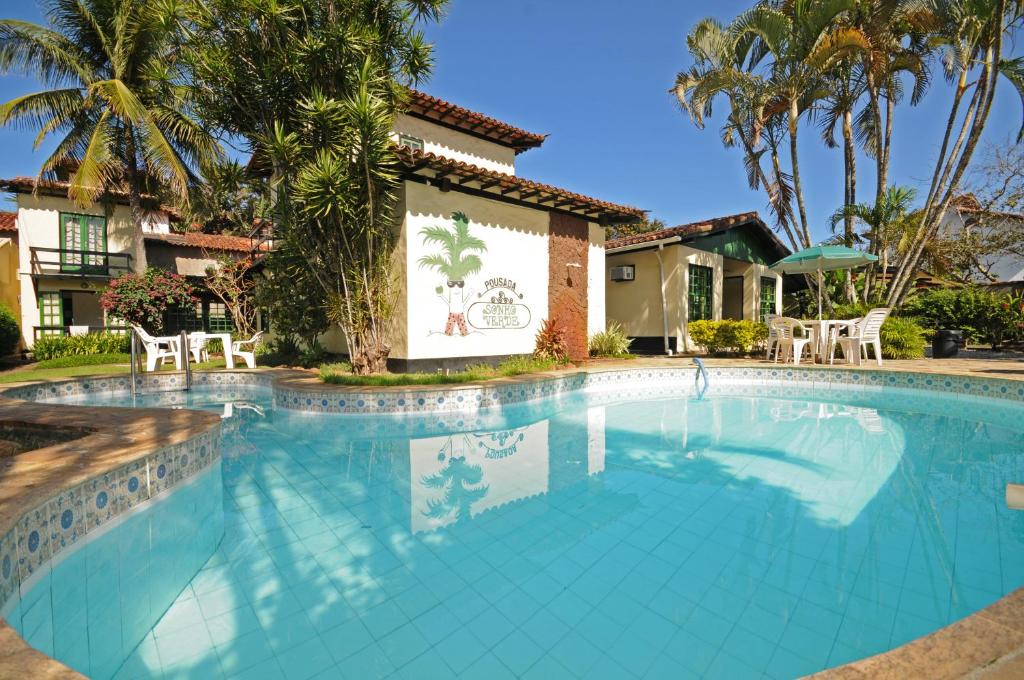 Parte da Pousada Sonho Verde que mostra a piscina azul ao ar livre com algumas árvores, parte da pousada e uma parede com a escrita do nome da pousada, ilustrando post Pousadas em Rio das Ostras.