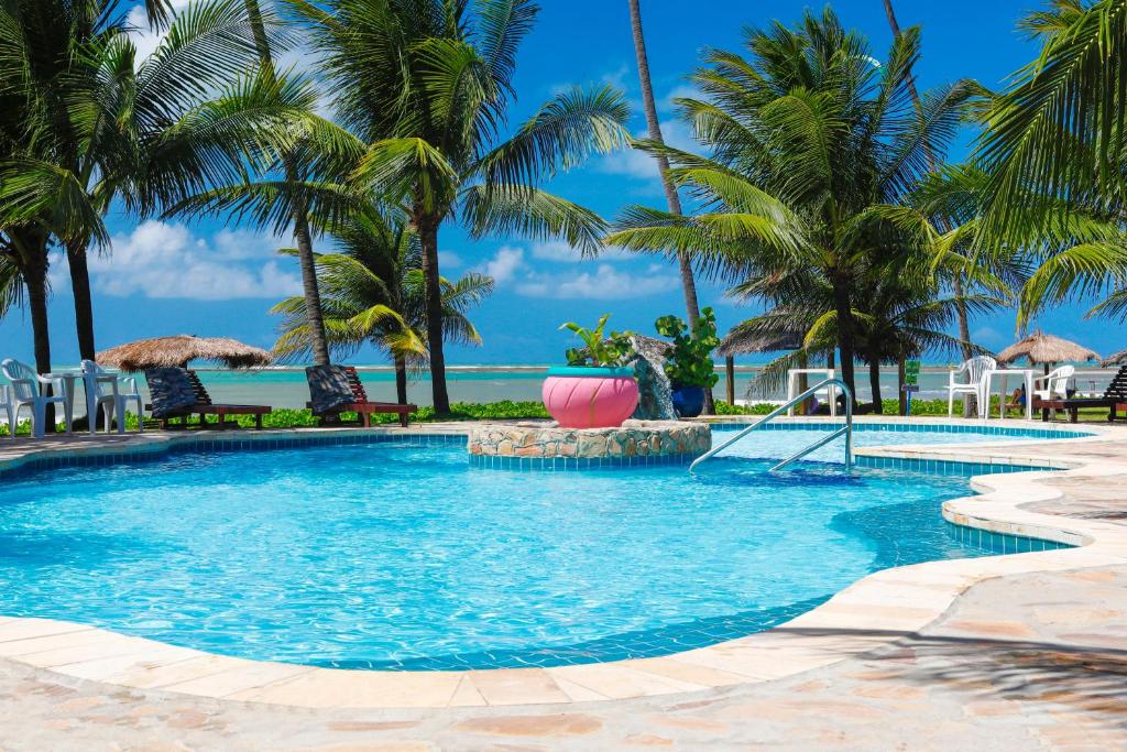 Piscina ao ar livre da Pousada Xalés de Maracaípe. Ao redor cadeiras, no fundo palmeiras e o mar.