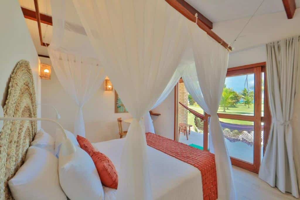 Quarto da Pousada Xalés de Maracaípe. Uma cama de casal do lado esquerdo, de frente uma porta de vidro com uma rede e a vista do jardim e mar. Foto para ilustrar post sobre pousadas em Ipojuca.