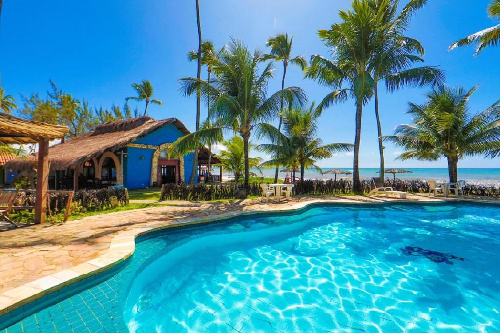 Uma das piscinas da Pousada Xalés de Maracaípe. Atrás da piscina se encontram coqueiros, mesas, cadeiras, um quiosque da pousada e a praia.