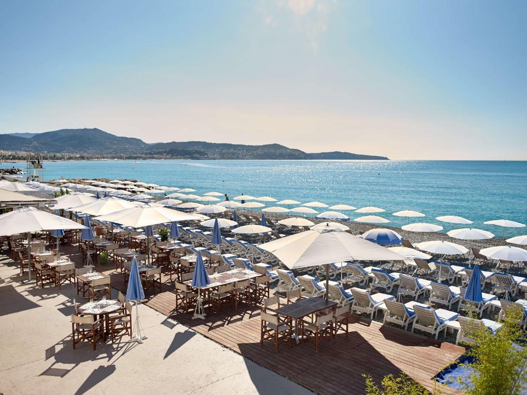 Praia privativa do Radisson Blu Hotel Nice. Há diversas mesas, cadeiras, espreguiçadeiras e guarda-sóis enfileirados em frente ao mar.