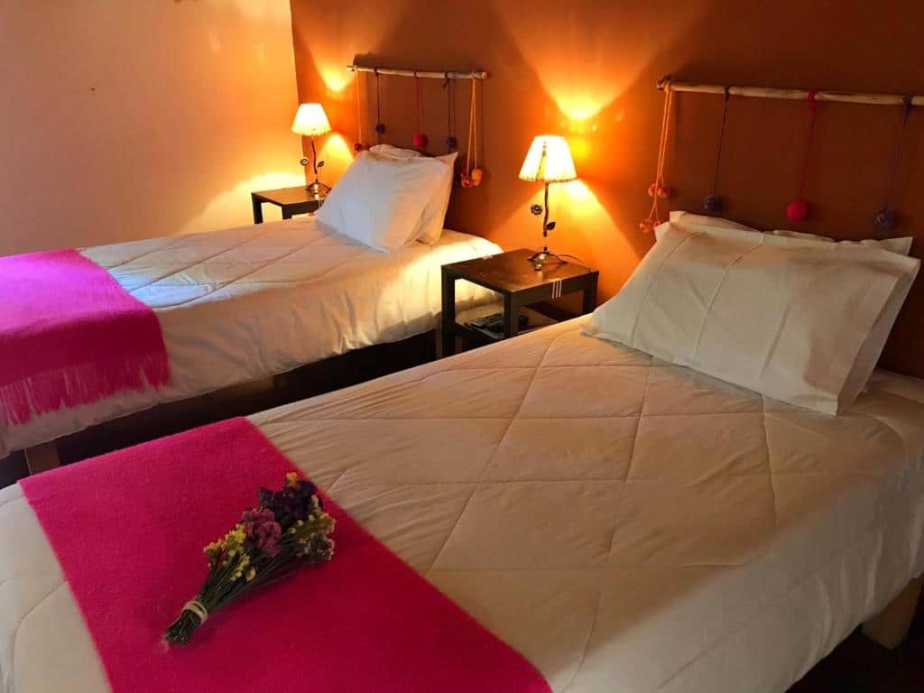 Quarto do Pumahuasi Hotel Boutique. Duas camas de solteiro no lado direito, entre elas e no fundo uma cômoda com abajur. Em cima da cama de solteiro na frente um buquê de flores. Foto para ilustrar post sobre hotéis em Jujuy.