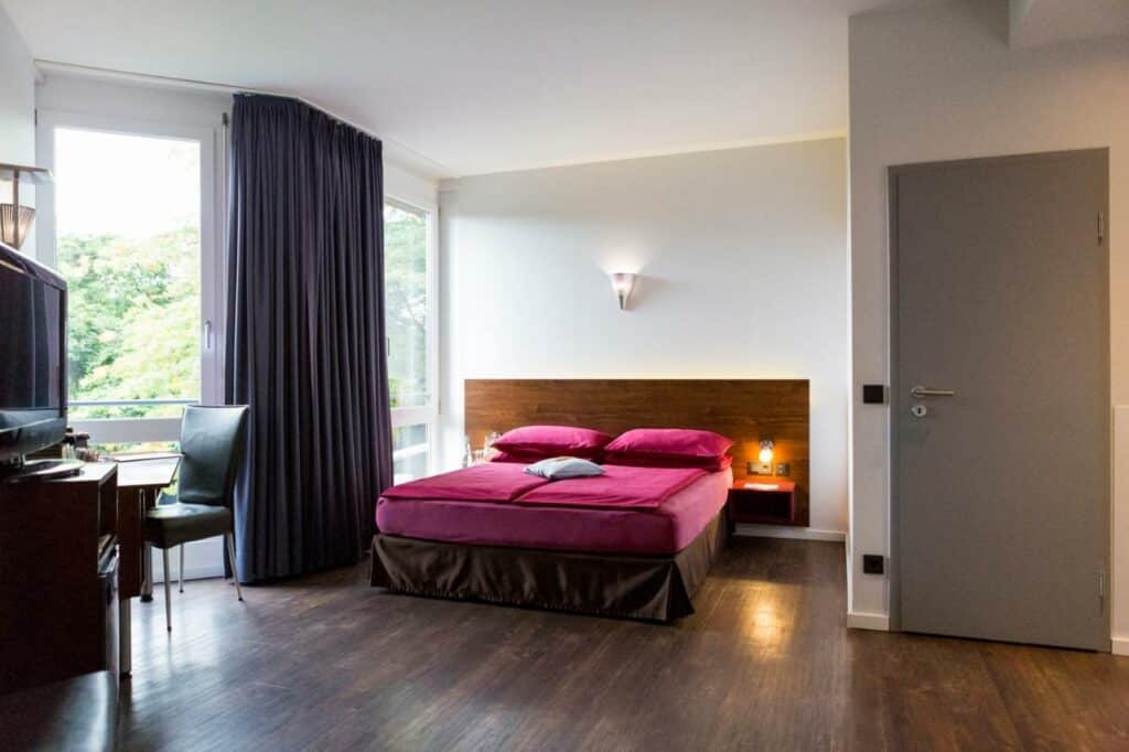 Quarto do Auszeit Hotel Düsseldorf – das Frühstückshotel – Partner of SORAT Hotels  com cama de casal no centro do quarto, do lado esquerdo da cama uma mesa de trabalho.  Representa hotéis em Dusseldorf.