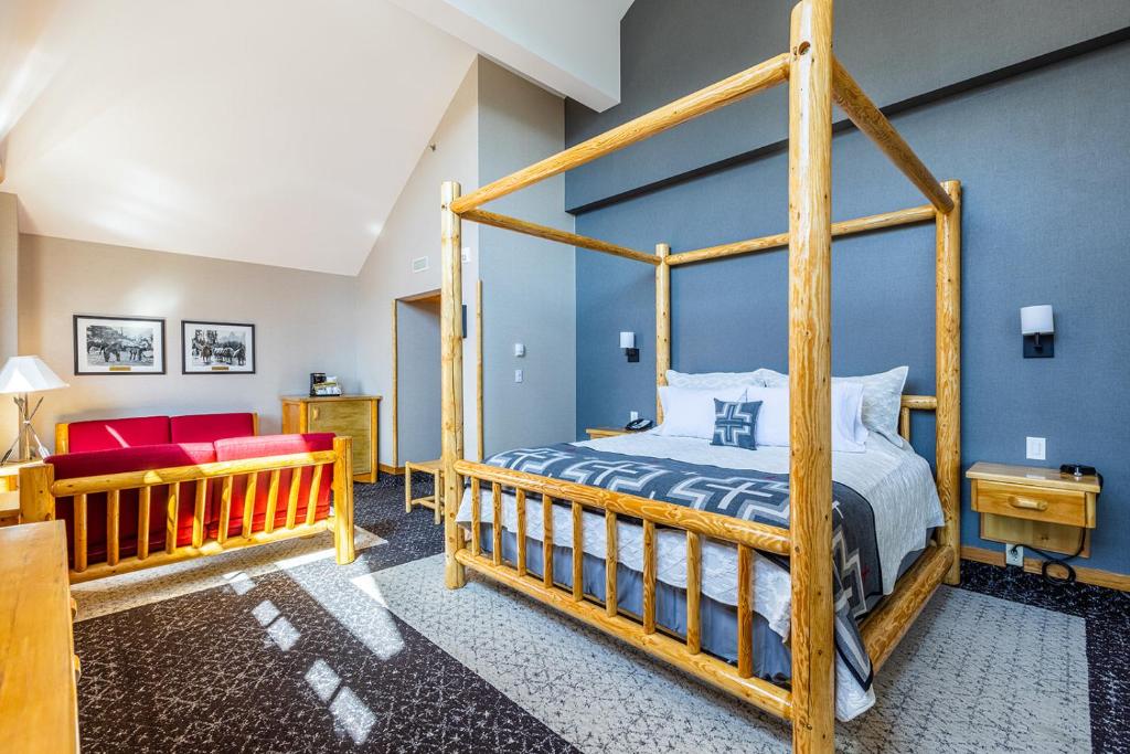 Quarto do Brewster Mountain Lodge com uma cama de casal com detalhes em madeira, de cada lado da cama tem uma mesinha de madeira com um telefone e o chão é de carpete. Além disso, na parte esquerda da foto tem dois sofás vermelhos com detalhes de madeira, dois quadros na parede, uma cômoda ao lado e uma porta aberta.
