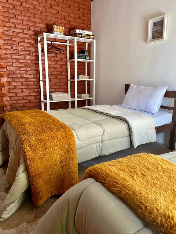 Foto de um quarto na Casa Charmosa, representando o post sobre pousadas em Nova Lima. Vemos uma cama de solteiro. Ao seu lado, há uma parede de tijolos e uma estante branca com toalhas, livros e cabides.