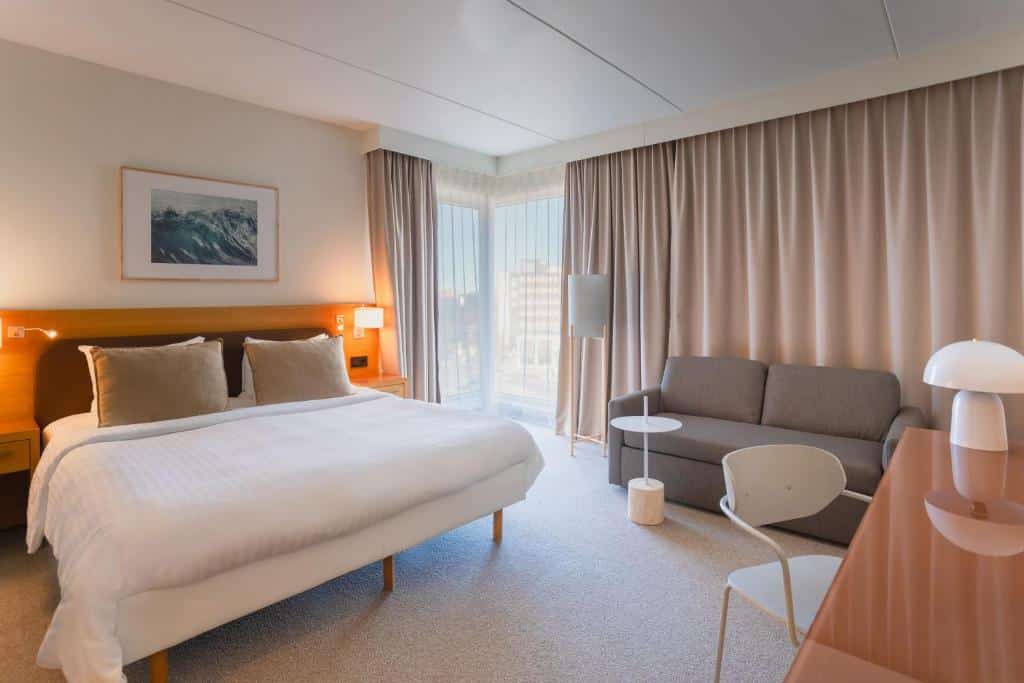 Quarto do Courtyard by Marriott Stockholm Kungsholmen com mesa com cadeira do lado direito da imagem, do lado esquerdo cama de casal e do lado esquerdo da cama um sofá. Representa hotéis em Estocolmo.