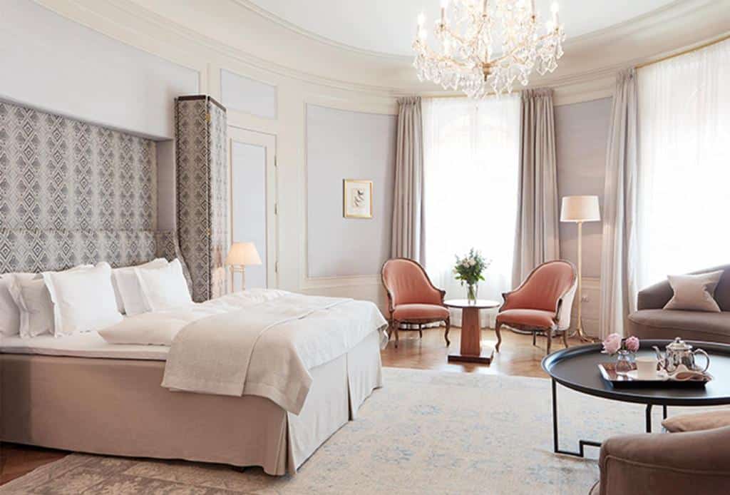 Quarto do Hotel Diplomat Stockholm com mesa redonda do lado direito da imagem, do lado esquerdo cama de casal e do lado esquerdo da cama duas poltronas com uma pequena mesa redonda. Representa hotéis em Estocolmo.