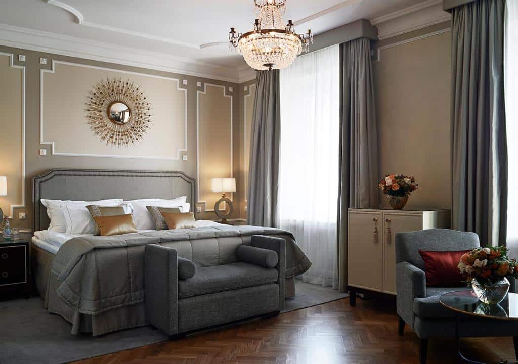 Quarto do Grand Hôtel Stockholm com cama de casal do lado esquerdo da imagem, com uma cômoda de cada lado com luminária, no pé da cama um pequeno sofá e a frente uma poltrona com uma mesinha redonda. Representa hotéis em Estocolmo.