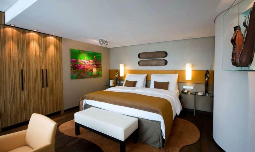 Quarto do Hotel Kö59 Düsseldorf – Member of Hommage Luxury Hotels Collection com cama de casal no centro do quarto e uma poltrona no pé da cama. Representa hotéis em Dusseldorf.