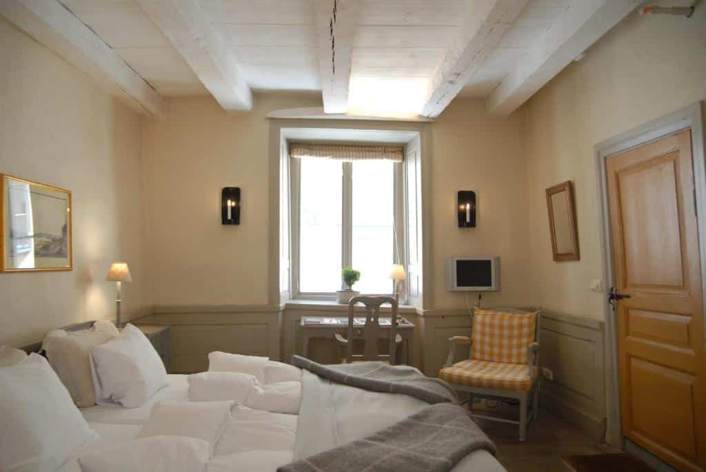 Quarto do Hotel Sven Vintappare com cama de casal do lado esquerdo da imagem, do lado esquerdo da cama uma cômoda com luminária, um pouco mais a frente uma mesa com cadeira.  Representa hotéis em Estocolmo.