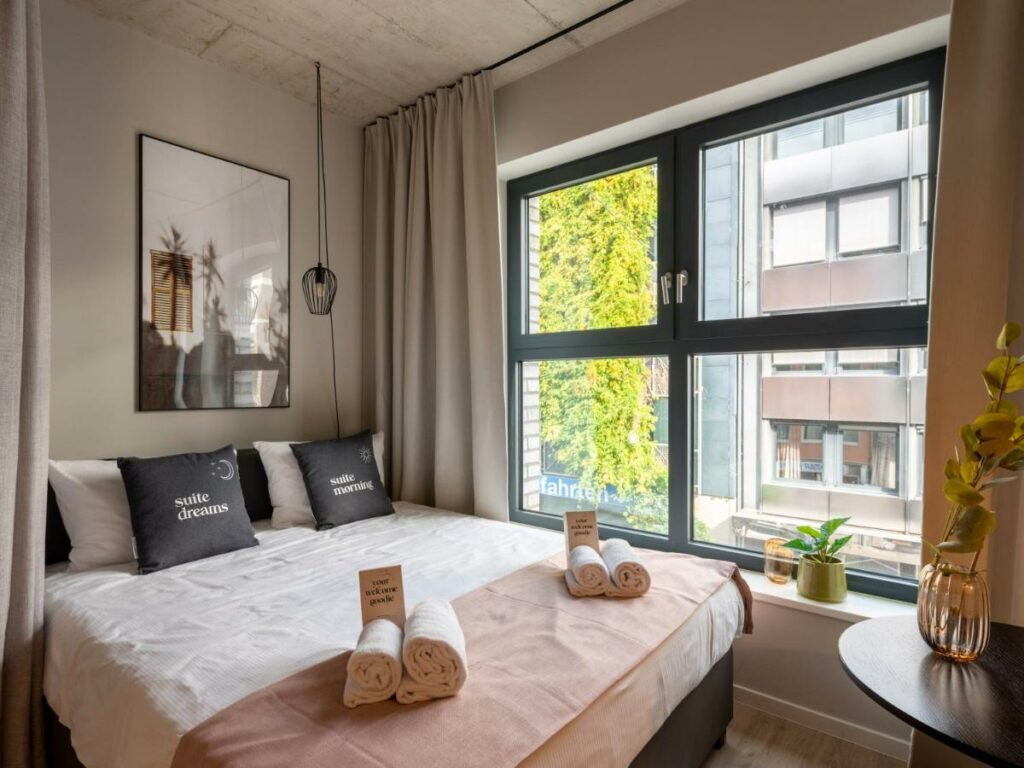 Quarto do limehome Düsseldorf Stresemannstraße – Digital Access com cama de casal do lado esquerdo da imagem e uma mesa redonda a frente da cama. Representa hotéis em Dusseldorf.