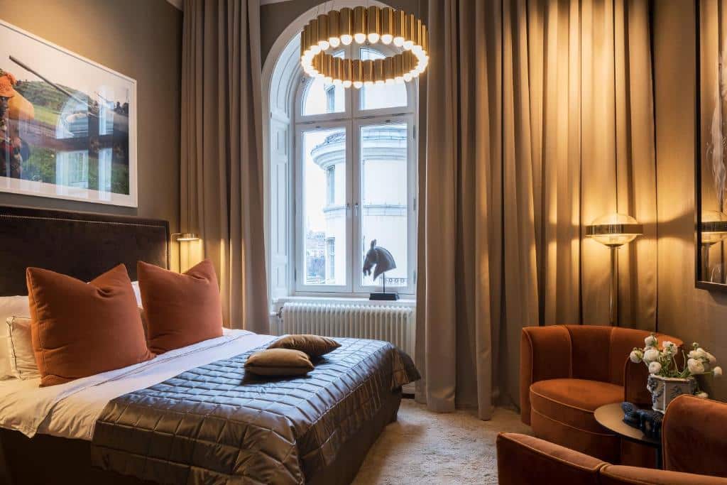 Quarto do Lydmar Hotel com duas poltronas com uma mesa redonda do lado direito da imagem, do lado esquerdo uma cama de casal. Representa hotéis em Estocolmo.