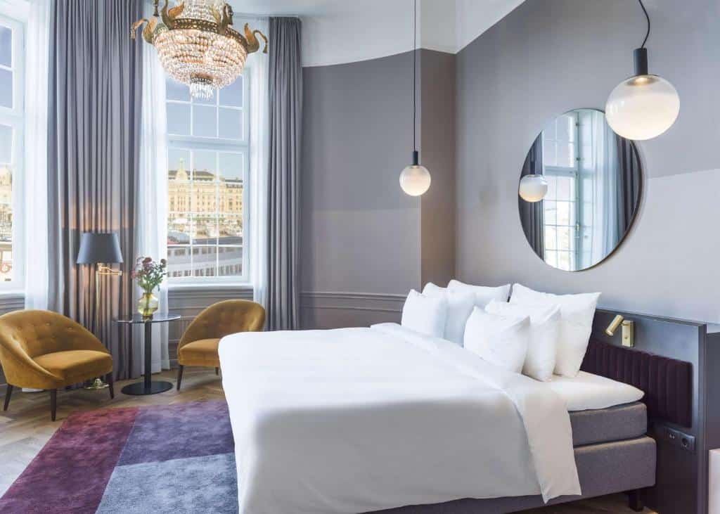 Quarto do Radisson Collection, Strand Hotel, Stockholm com cama de casal do lado direito da imagem, do lado esquerdo da imagem duas poltronas com uma mesa redonda ao meio. Representa hotéis em Estocolmo.