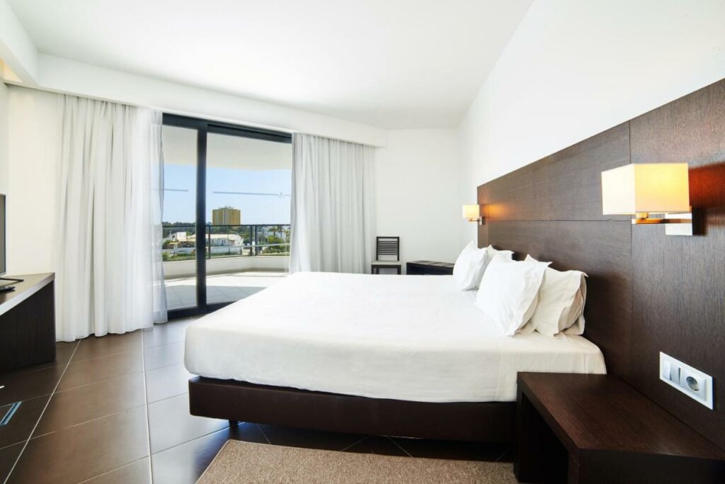 Quarto do RR Alvor Baía Resort com cama de casal do lado direito da imagem em frente a cama uma cômoda. Representa hotéis all inclusive em Portugal.