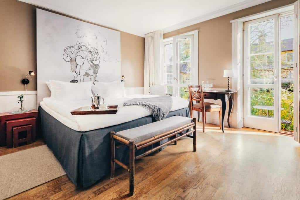 Quarto do Stallmästaregården Hotel, Stockholm, a Member of Design Hotel com cama de casal do lado esquerdo da imagem, com uma cômoda do lado direito da cama, do lado esquerdo da cama uma mesa com cadeira e no pé da cama um banco estofado.