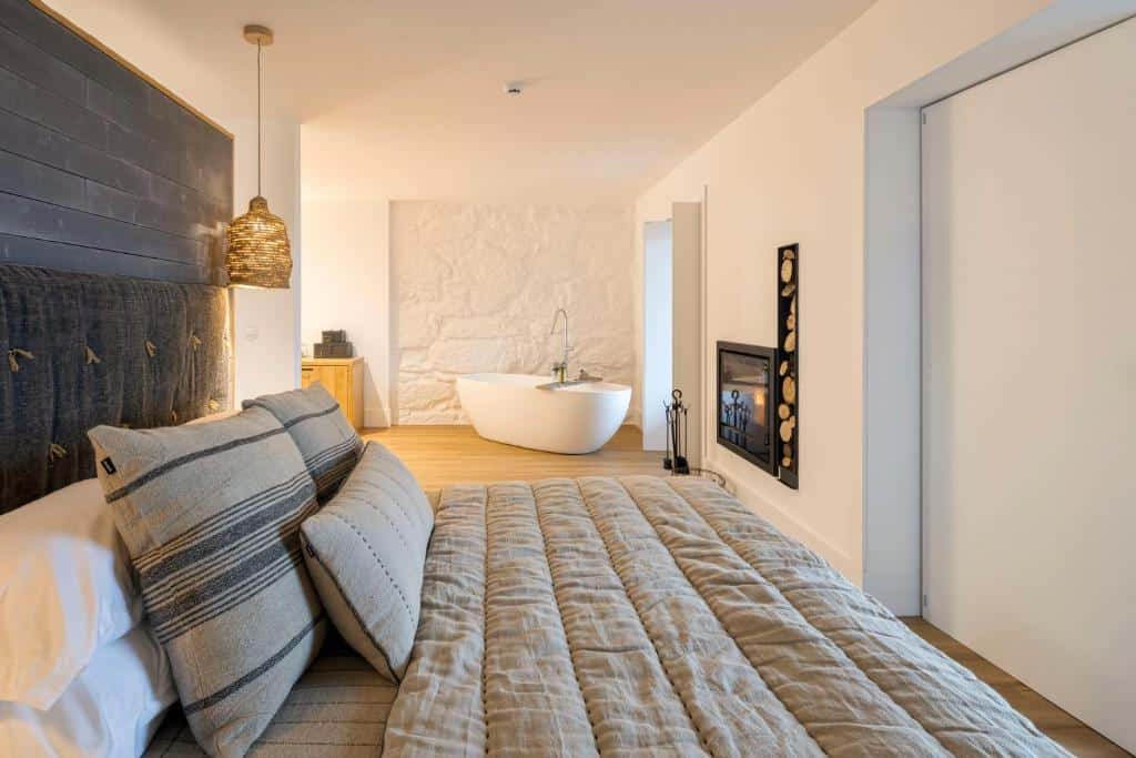 Quarto do TheVagar Countryhouse com cama de casal do lado esquerdo da imagem e ao fundo lareira e uma banheira de hidromassagem. Representa hotéis para lua de mel em Portugal.