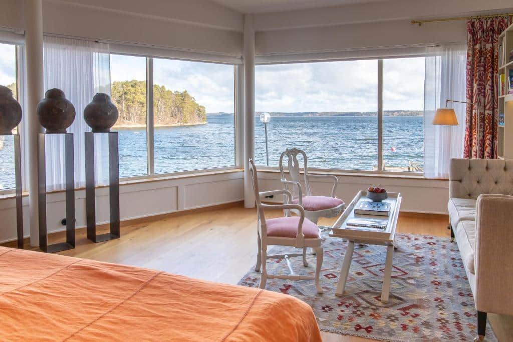Quarto do Vår Gård Saltsjöbaden  com cama de casal do lado esquerdo da imagem no canto com vista para o mar, do lado direito sofá com mesa de centro e duas cadeiras.