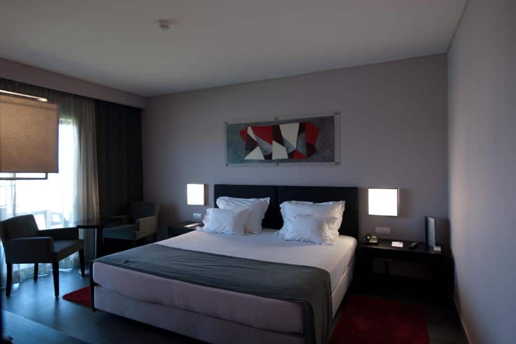 Quarto do Vila Gale Lagos com cama de casal no centro da imagem com duas cômodas em cada lado da cama e do lado esquerdo da cama duas poltronas. Representa hotéis all inclusive em Portugal.
