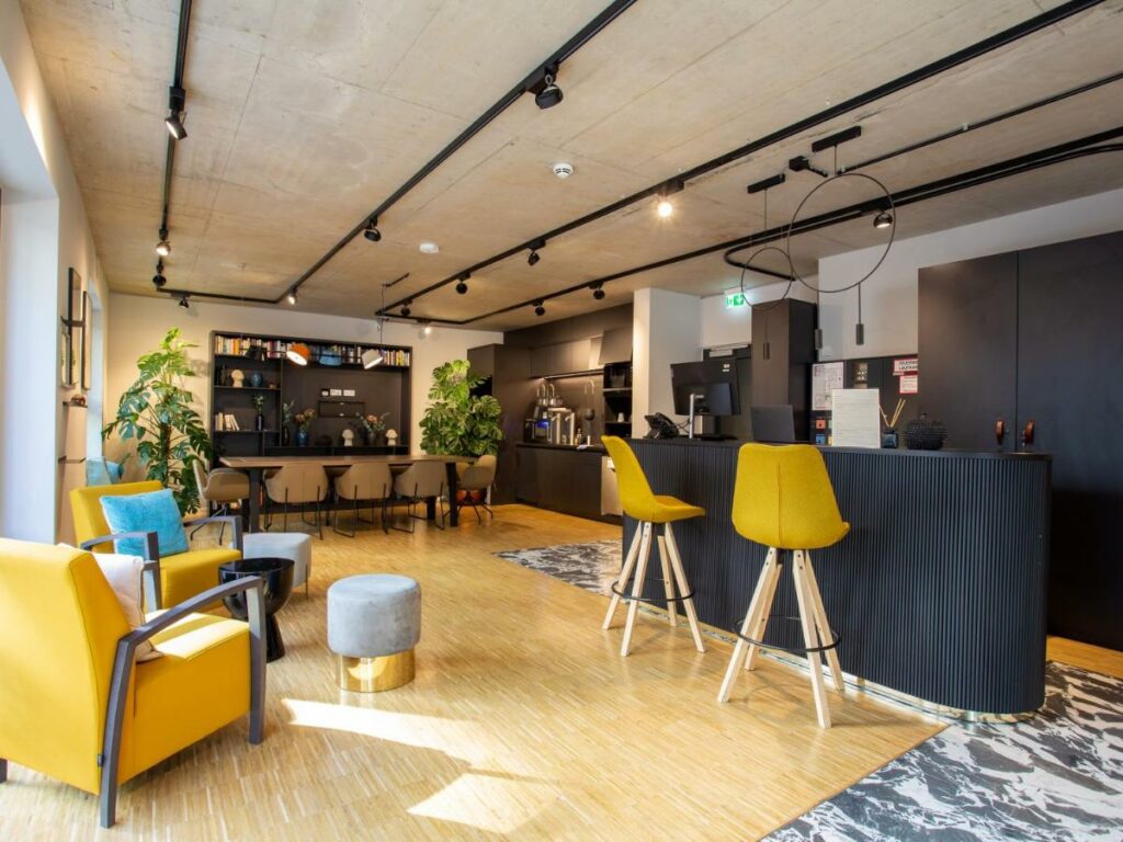 Recepção do limehome Düsseldorf Stresemannstraße – Digital Access com balcão de atendimento do lado direito da imagem com duas cadeiras altas a frente do lado esquerdo da imagem poltronas.