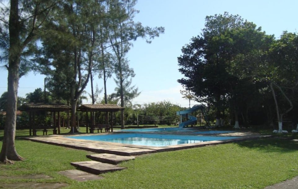 Piscina ao ar livre do Samburá Chalés. Três piscinas com um tobogã no meio. Ao redor, árvores. No fundo, um campo.