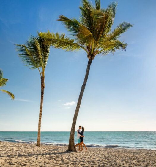 Casal dançando ao lado de uma palmeira no Sanctuary Cap Cana, um dos melhores hotéis para lua de mel em Punta Cana. O sol brilha ao lado de outra árvore ali, e há mais delas ao redor.