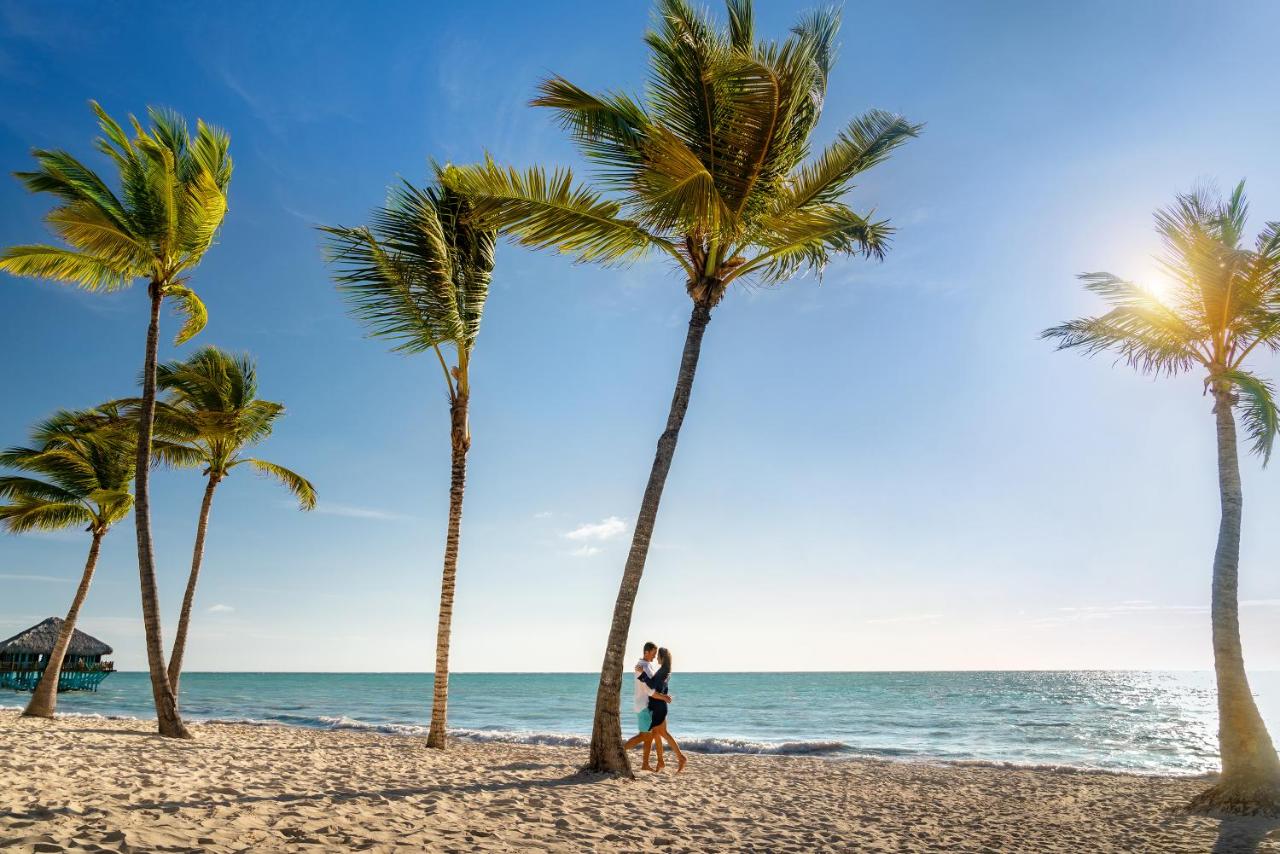Casal dançando ao lado de uma palmeira no Sanctuary Cap Cana, um dos melhores hotéis para lua de mel em Punta Cana. O sol brilha ao lado de outra árvore ali, e há mais delas ao redor.