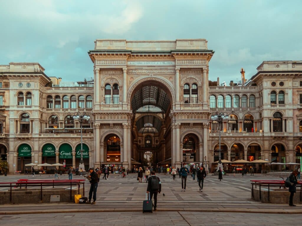 Galleria Vittorio Emanuele II, em Milão, na Itália, com fachada imponente de arquitetura trabalhada, e pessoas andando em frente