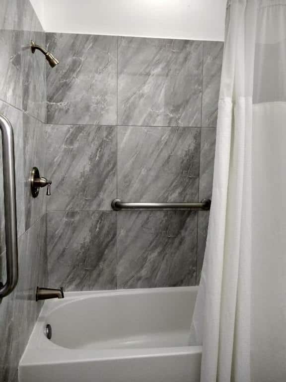 Banheiro com barras de apoio no The Great House Inn. Na foto vemos a banheira com uma ducha que possui barras de apoio ao seu redor.