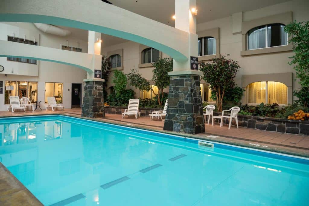 Parte do The Rundlestone Lodge que mostra a piscina em um local coberto, com duas pilastras formando dois arcos em cima da piscina. Em volta tem algumas cadeiras e espreguiçadeiras e também algumas plantas, ilustrando post Hotéis em Banff.