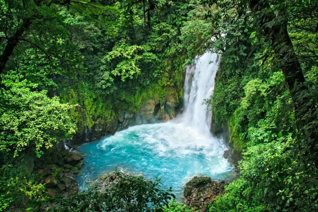 Uma queda d'água como uma pequena cachoeira em azul claro cercado por árvores e pedras