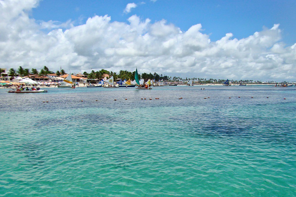 Praia de Porto de Galinhas, água cristalina e no fundo barcos a vela e a praia.