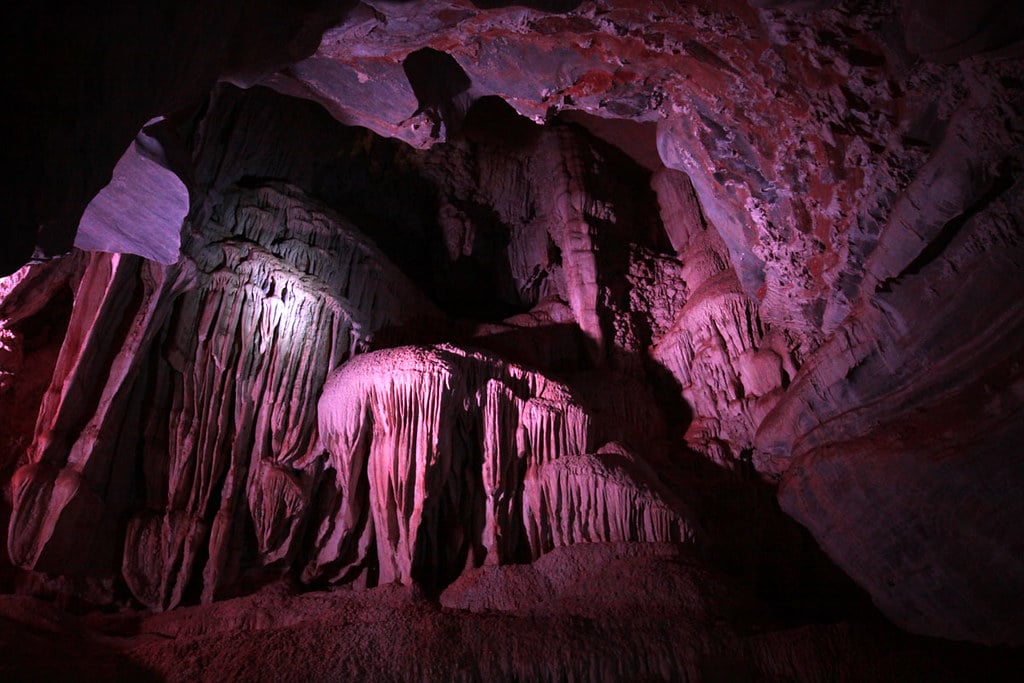 Interior da Gruta da Lapinha. Ela está iluminada por uma luz roxa e é possível ver diversas formações pontiagudas.