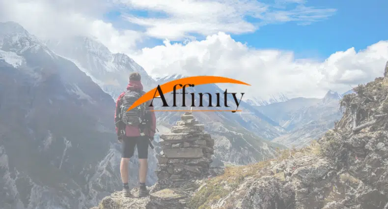 Um homem no alto de uma montanha observando outras montanhas com nuves baixas e vegetação no local, para representar Affinity Seguro Viagem