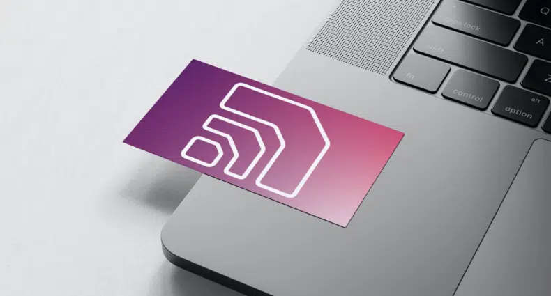cartão com o logo da America Chip em cima de um notebook aberto em cima de uma mesa. O cartão tem tons de rosa e roxo e está com o símbolo branco de uma rede de internet