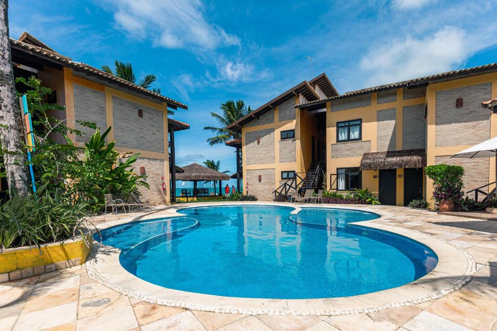 Piscina ao ar livre do Anauí Pousada. Do lado esquerdo e do lado direito a pousada, no fundo um guarda-sol de palha e a praia.