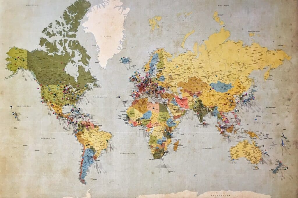 Foto de um mapa mundi preso em uma parede e nele há diversos pininhos coloridos presos