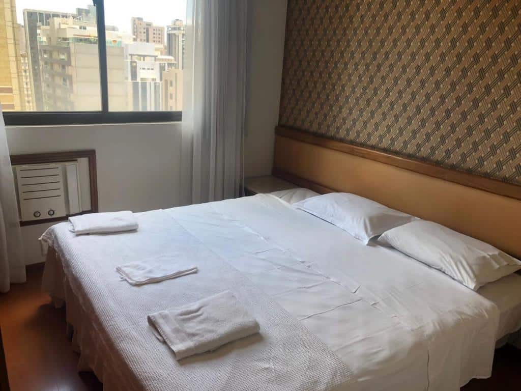 Quarto do apart Hotel Volpi. A cama é box de casal e está encostada na parede na direita. Há uma cabeceira atrás. A janela está do lado direito da cama. Representa o post de airbnb em Belo Horizonte.