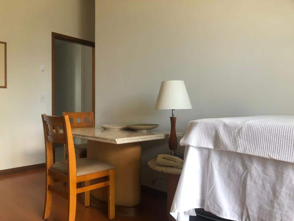 Uma mesa com duas  cadeiras e um abajur na frente da cama do apart Hotel Volpi.