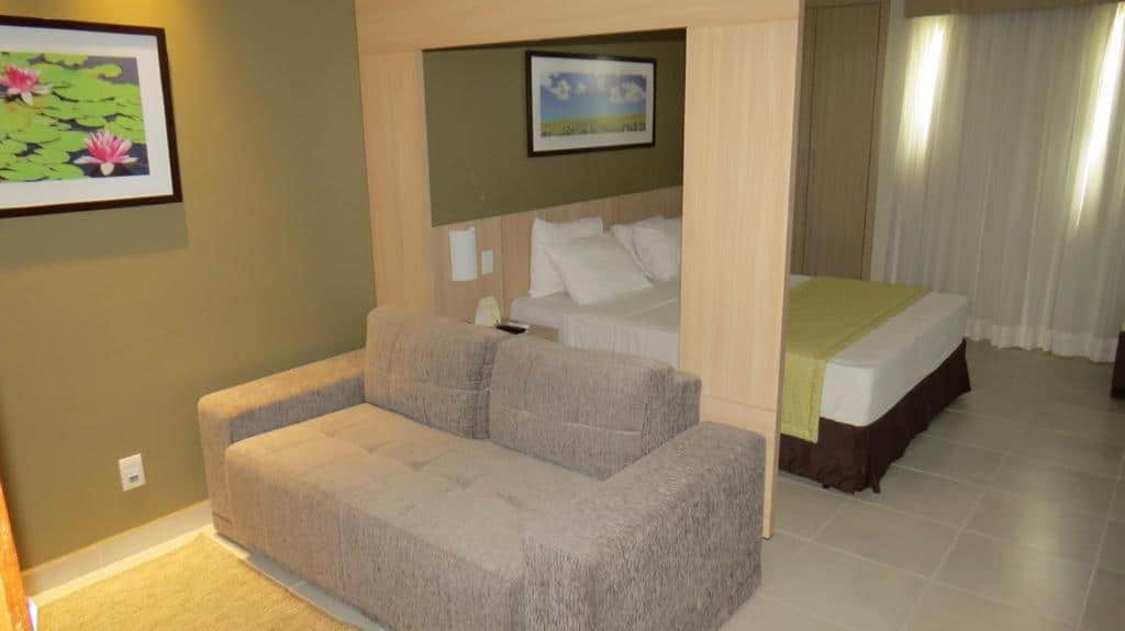 Quarto do Apartamentos Caldas Novas. Um sofá na frente, atrás uma pilastra e uma cama de casal. Foto para ilustrar post sobre airbnb em Caldas Novas.