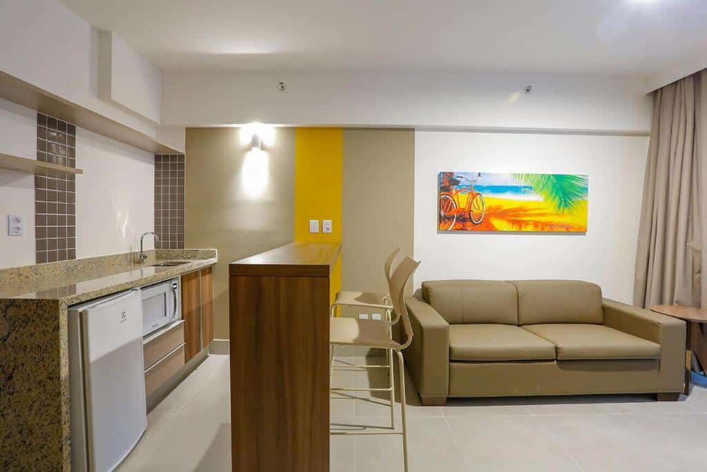 Do lado direito uma minicozinha, no meio um balcão com dois bancos, do lado direito um sofá no Apartamento em Resort de Olimpia.