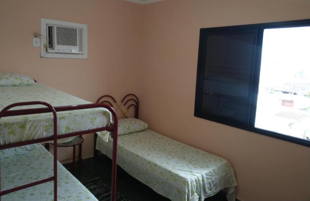 Quarto do Apartamento em Ubatuba. Do lado esquerdo uma cama beliche, do lado direito uma cama de solteiro, em cima uma janela.