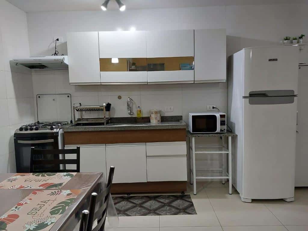 Cozinha do Apê no centro com Varanda Gourmet. Do lado esquerdo uma mesa, no fundo um fogão com centrifuga, o armário no meio com a pia e o micro-ondas, e do lado direito a geladeira.