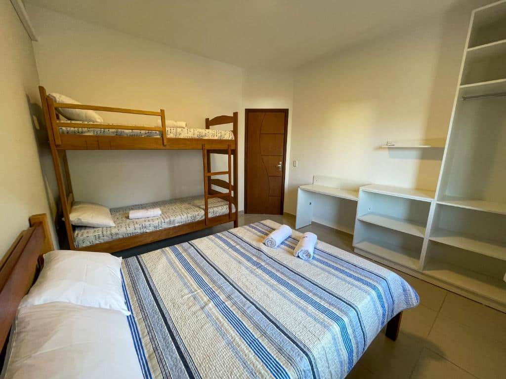 Quarto do Apto Funcional próximo a Orla do Centro HS4. Uma cama de casal e uma cama de beliche do lado esquerdo. De frente a porta do quarto e um armário. Foto para ilustrar post sobre airbnb no centro de Ubatuba.