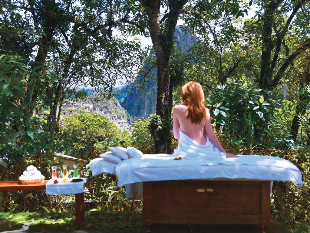 mulher branca de cabelos ruivos sentada em cima de uma maca de massagem com as costas nuas, olhando para as ruínas da cidade de Machupicchu ao fundo, escondida pela vegetação verde ao redor