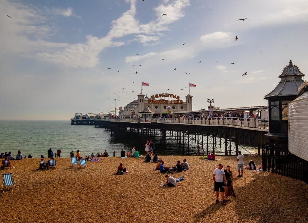 Um pier em Brighton na Inglaterra com atrações de parques de diversão montanhas, na areia há pessoas sentadas e andando, para representar seguro viagem Inglaterra