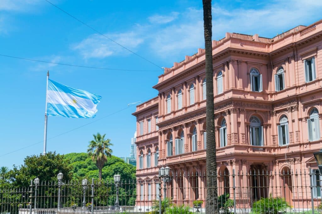 Um prédio histórico rosada em Buenos Aires na Argentina, em frente ao local há algumas árvores e uma bandeira da Argentina