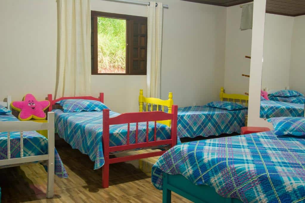 Quarto do Cantinho na Roça. Do lado direito uma cama de solteiro, no fundo outras três camas de solteiro e uma janela do quarto. Foto para ilustrar post sobre airbnb em Santo Antônio do Pinhal.