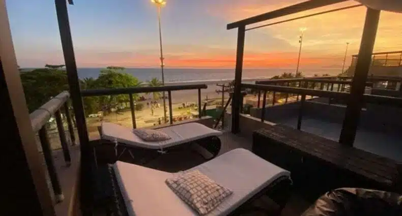 Varanda do AP Pepê ALECRIM com JACUZZI e SOLÁRIO Frente ao MAR no final do dia com cadeiras a frente e ao fundo vista do mar. Representa airbnb na Barra da Tijuca.