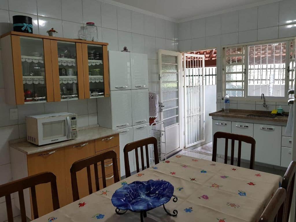 Cozinha da "Casa da Cachoeira" com uma mesa com seis cadeiras, três armários do lado esquerdo da foto e ao fundo uma pia com armário e uma porta aberta. Imagem ilustrando post Airbnb em Brotas.