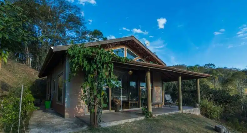 Área externa da Casa da Montanha para ilustrar post sobre airbnb em Santo Antônio do Pinhal. Ao redor as montanhas, no meio a casa com varanda.